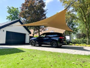 Zandkleurige stretchtent als carport in tuin met bomen en grasveld
